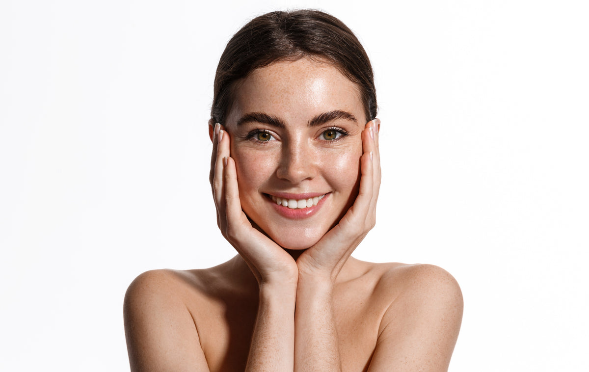 “Woman with bare shoulders gently applying facial serum to clean skin against a white background”
