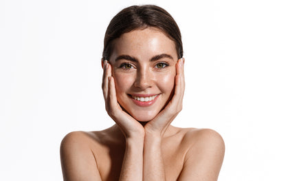 “Woman with bare shoulders gently applying facial serum to clean skin against a white background”